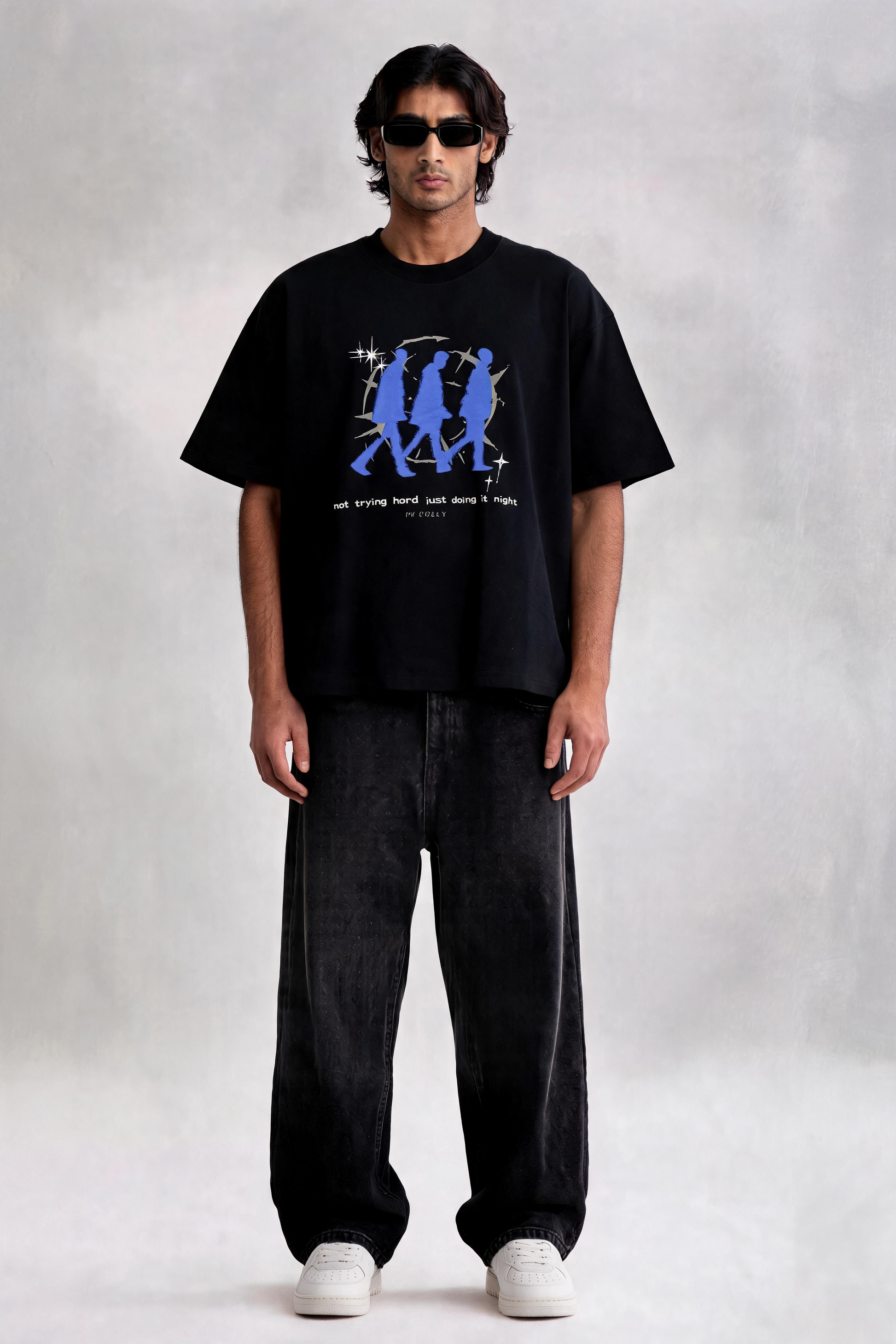 Man wearing a black t-shirt with a blue graphic and text, standing against a plain background