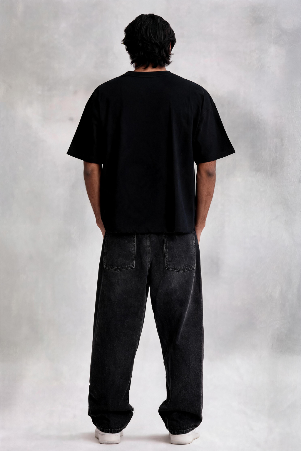 Person wearing a black t-shirt and dark jeans standing against a plain background
