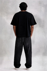 Person wearing a black t-shirt and dark jeans standing against a plain background