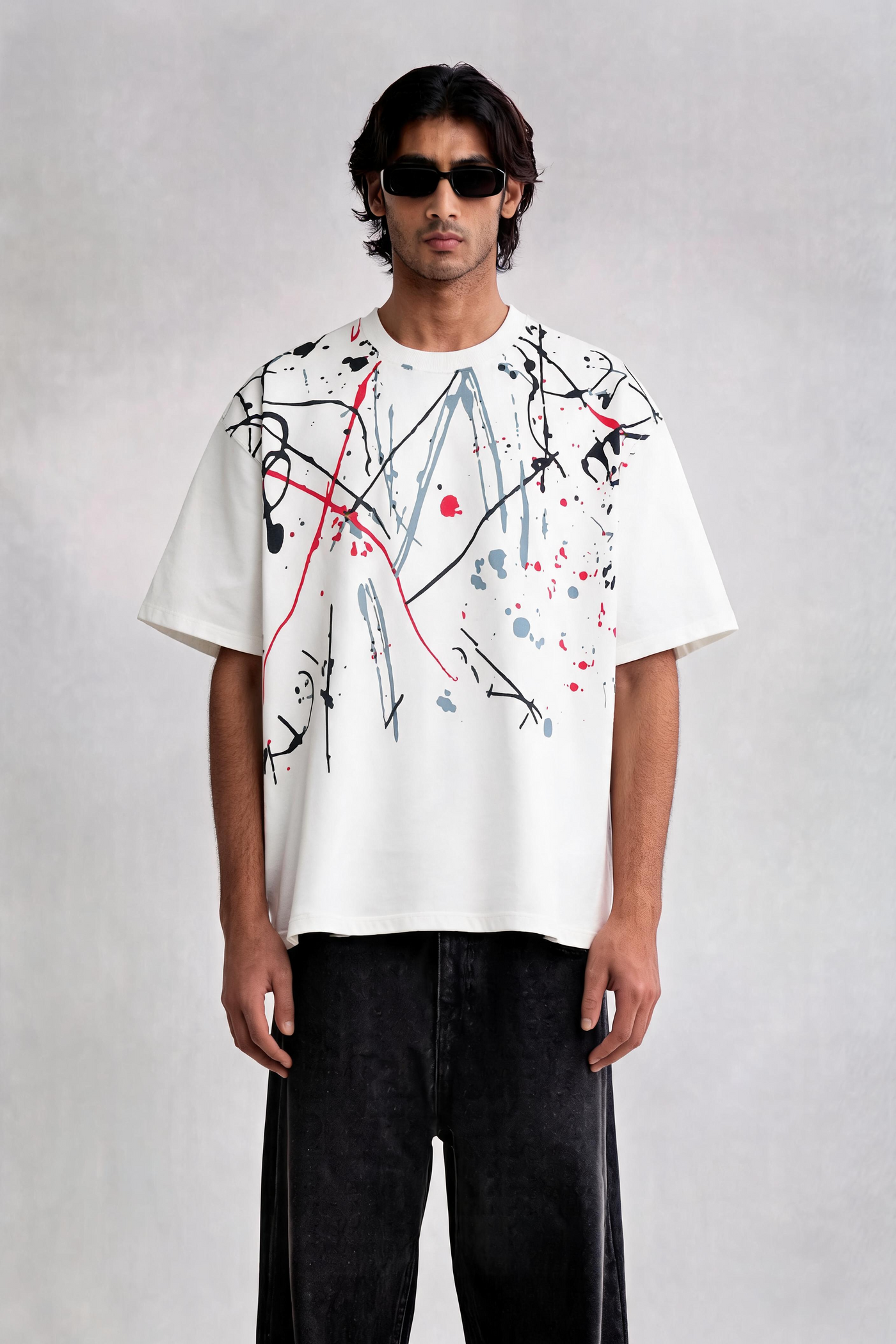 Man wearing a white t-shirt with abstract designs and dark pants on a plain background