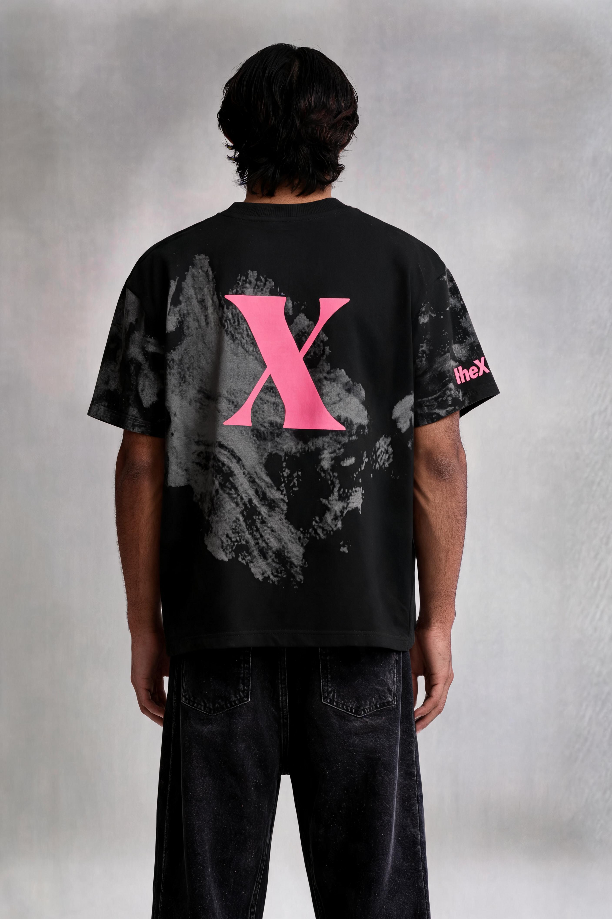 Person wearing a black t-shirt with a pink 'X' on the back against a gray background