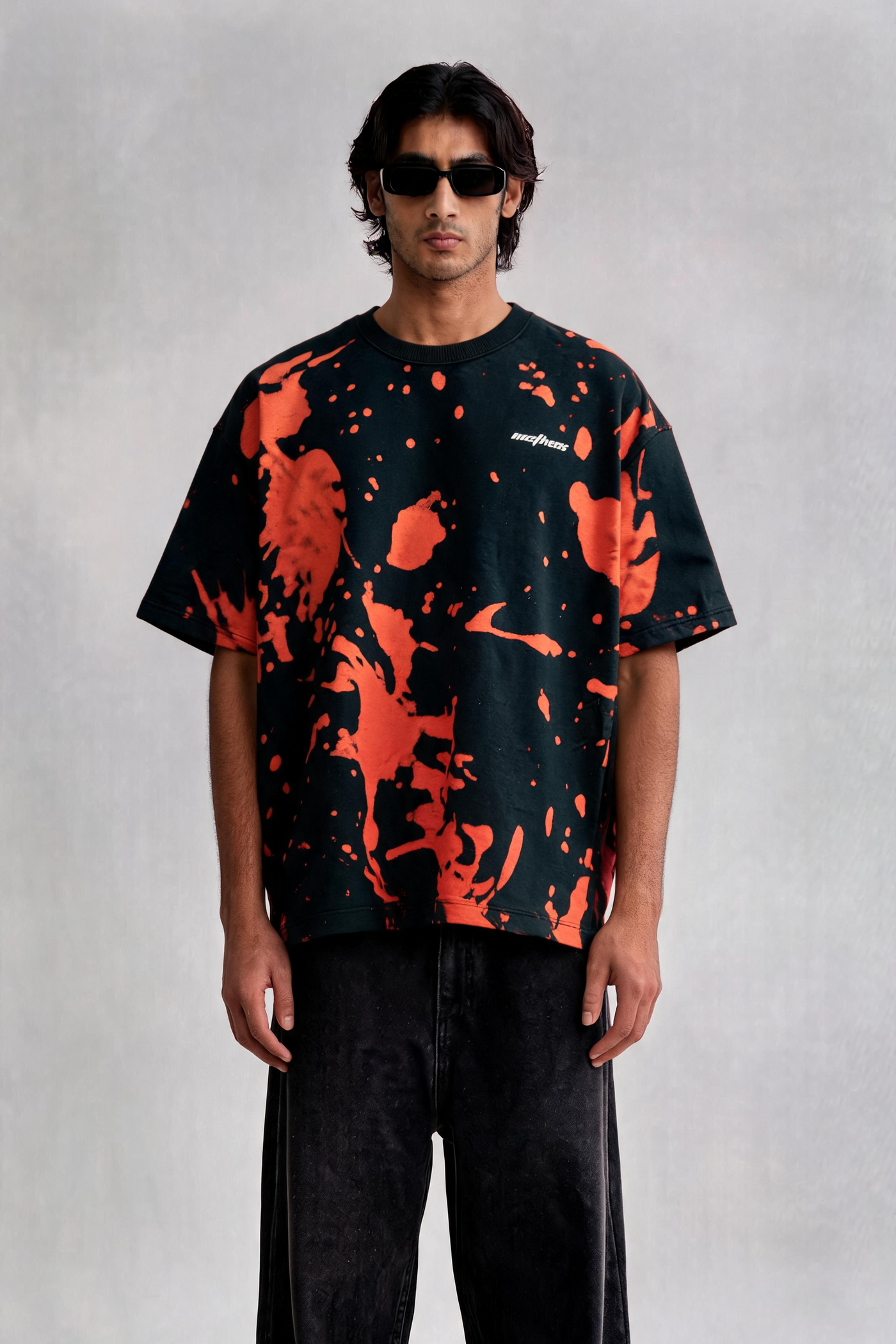 Person wearing a black and orange splatter pattern t-shirt with dark pants on a light gray background