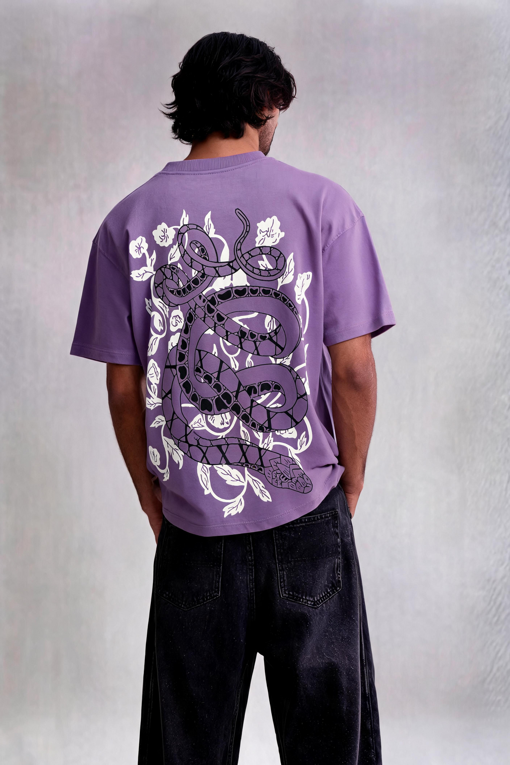 Person wearing a purple t-shirt with a white graphic design on the back, standing against a plain background.