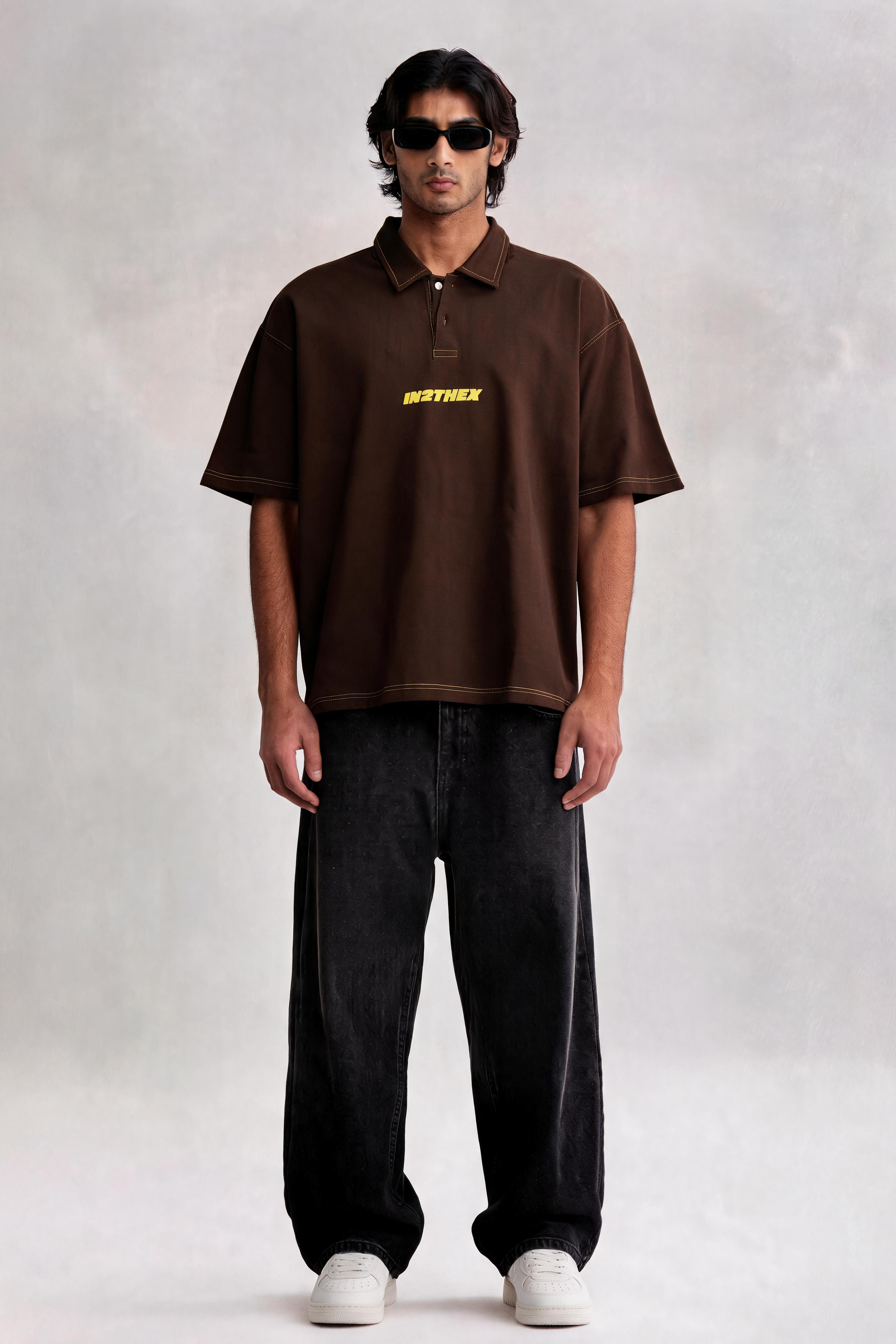 Man wearing a brown polo shirt with a logo, black pants, and white shoes on a plain background