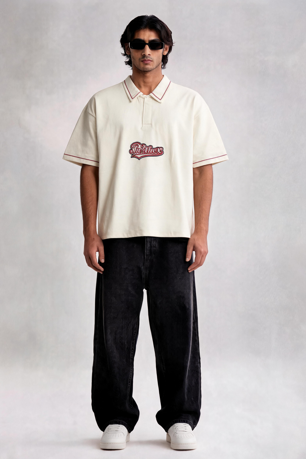 Man wearing a cream-colored polo shirt with a logo and dark pants on a plain background